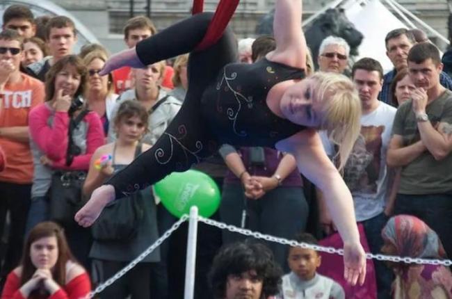 An acrobat dancer dangles from the air while dancing for an audience. 