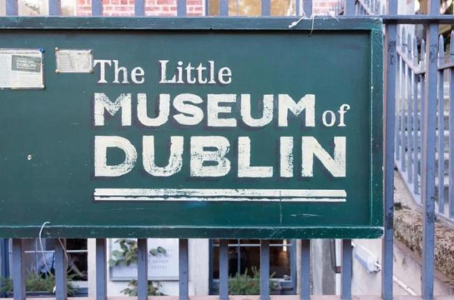 A faded green sigh on a fence that thats The Little Museum of Dublin.